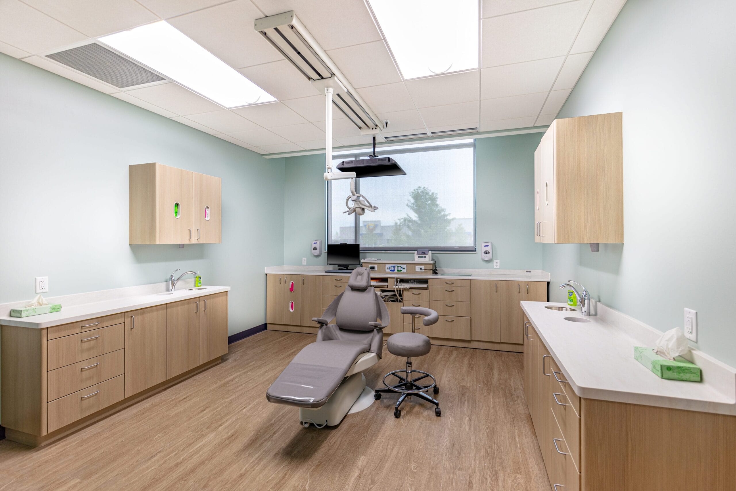 Modern dental office featuring a treatment chair, cabinetry, and large window with natural light.