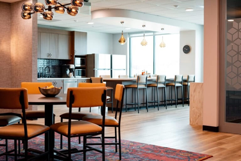 Modern kitchen and dining area featuring orange chairs, a round table, and a sleek bar with pendant lighting.