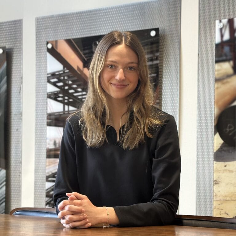 Young woman with long blonde hair, wearing a black shirt, sits at a table.